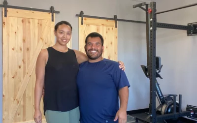 Two individuals smiling together in a fitness studio setting, showcasing a supportive environment for physical therapy and wellness services.