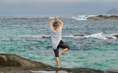 Woman practicing yoga in tree pose on rocky beach, emphasizing balance and wellness in natural setting, relevant to health and fitness discussions.