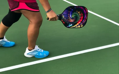 Person in athletic wear holding a colorful pickleball paddle on a green court, illustrating the connection between pickleball and physical fitness.