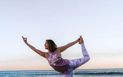 Woman practicing yoga on the beach, demonstrating a balance pose at sunset, promoting wellness and physical health.