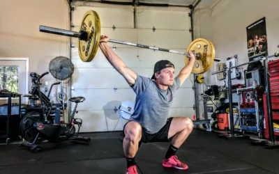 Man performing overhead squat with barbell in a gym setting, demonstrating strength training and physical fitness techniques relevant to rehabilitation and performance enhancement.